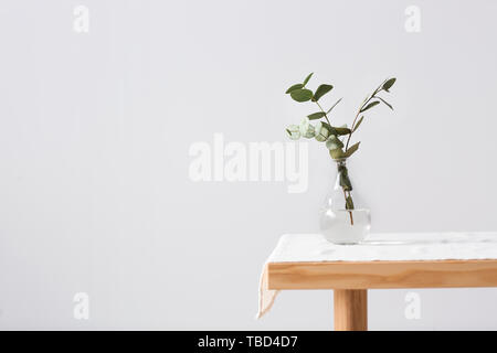 Vase with fresh eucalyptus branches on table against light background Stock Photo