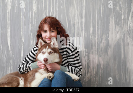 Young woman with her cute dog near grey wall Stock Photo