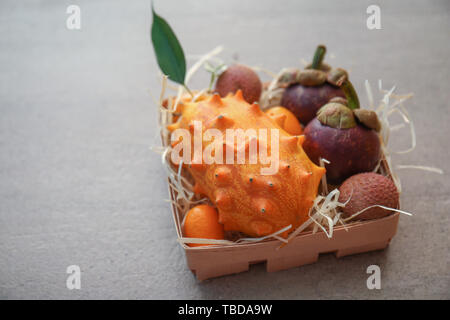 Box with assortment of tasty exotic fruits on grey background Stock Photo