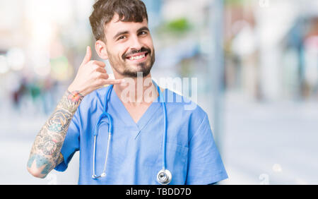 Young handsome nurse man wearing surgeon uniform over isolated background smiling doing phone gesture with hand and fingers like talking on the teleph Stock Photo