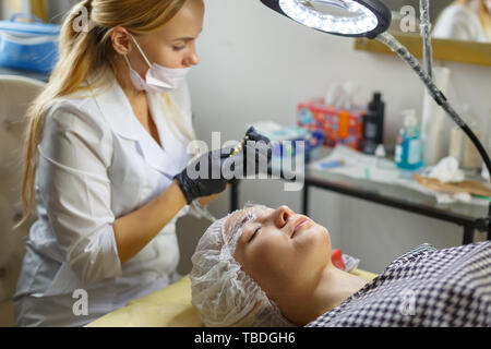 Microblading eyebrows work flow in a beauty salon. Woman having her eye brows tinted. Semi-permanent makeup for eyebrows. Focus on model's face and ey Stock Photo