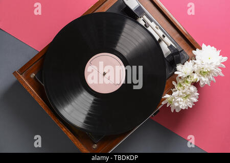 Record player with vinyl disc and flowers on color background Stock Photo