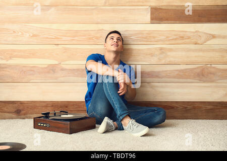 Young man listening to music on record player near wooden wall Stock Photo