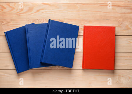 Red book among blue ones on wooden background. Concept of uniqueness Stock Photo