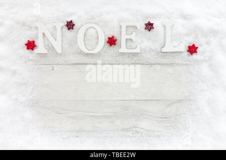Wooden Noel letters and red Christmas stars on snow and white, gray wood panel background with lots of copy space. Top view. Stock Photo