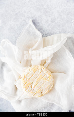 Top view of round goat cheese on white muslim cloth and textured background with copy space. Stock Photo