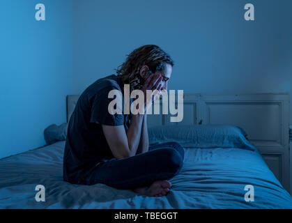Devastated millennial man crying sad feeling hurt and hopeless suffering Depression. Depressed teenager victim of bullying or abuse sitting on bed alo Stock Photo