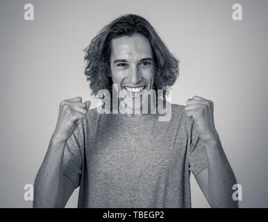 Portrait of very excited young man celebrating winning the lottery or having great success. Teenager with long hair and surprised and happy gestures.  Stock Photo