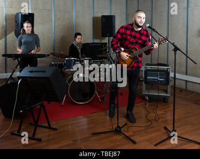 adult emotional guy with guitar rehearsing with female drummer and keyboardist before  public performance Stock Photo