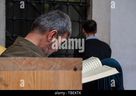 Sarajevo, Bosnia: a muslim man reading the Quran near a brother praying in the direction of Mecca outside the Gazi Husrev-beg Mosque (1532) Stock Photo