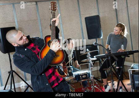 Bearded guy soloist playing the guitar and singing with two girls of his music band at studio Stock Photo