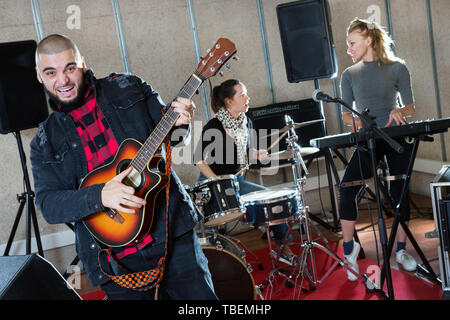 Bearded guy soloist playing guitar and singing with two girls of the his music band in studio Stock Photo