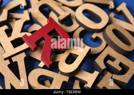 Red letter among wooden ones on color background, closeup. Concept of uniqueness Stock Photo