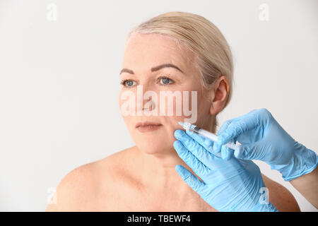 Mature woman receiving injection in face on light background Stock Photo