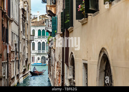 Gondolier in a stripped vest floating on a gondola through a narrow channel among the cozy italian houses in Venice Stock Photo