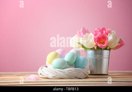 Nest with Easter eggs and flowers on table against color background Stock Photo