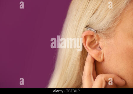 Mature woman with hearing aid on color background, closeup Stock Photo