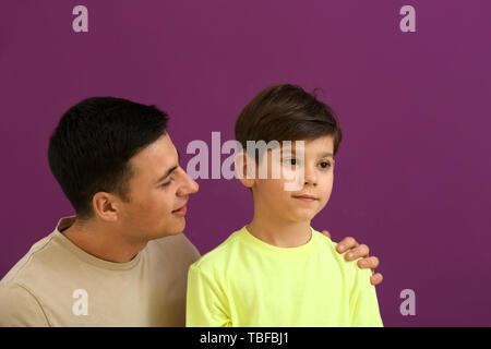 Young man and his son with hearing aid on color background Stock Photo