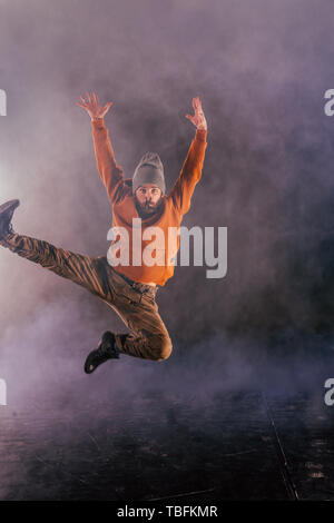 Male breakdancer jumps off high in the air while performing a cool dance move, a lot of smoke in the background. Stock Photo
