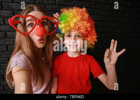 Woman and little girl in funny disguise on dark background. April fools' day celebration Stock Photo