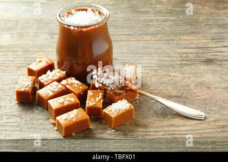 Tasty salted caramel in jar with candies on wooden table Stock Photo