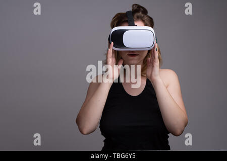 Young woman touching VR googles. Isolated against gray background Stock Photo