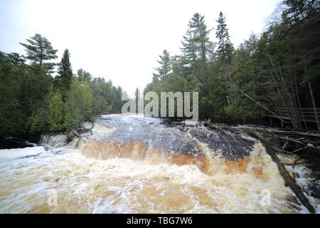 Short, fast flowing waterfall with tea colored water churning up lots of foam Stock Photo