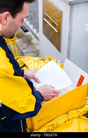 Postman delivering letters to mailbox of recipient Stock Photo