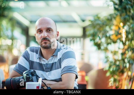 Freelance concept. Professional photographer. Young bearded man using laptop while sitting on summer terrace. Stock Photo