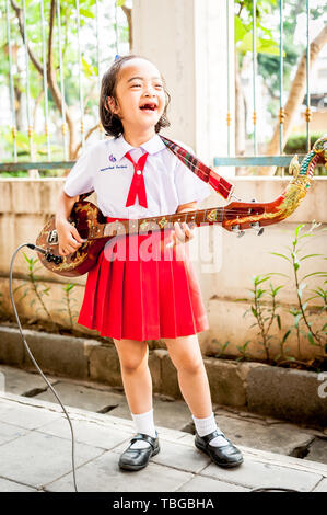 A cute little Thai girl performs to the public by playing her guitar in Bangkok Thailand. Stock Photo