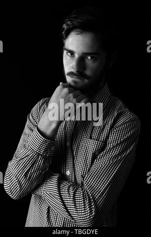 Young adult male looking sinister or contemplative. Monotone, black and white for dramatic effect, dark and moody series. Concept image for corporate  Stock Photo