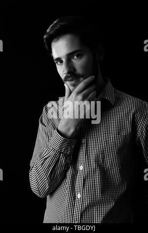 Young adult male looking sinister or contemplative. Monotone, black and white for dramatic effect, dark and moody series. Concept image for corporate  Stock Photo