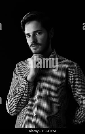 Young adult male looking sinister or contemplative. Monotone, black and white for dramatic effect, dark and moody series. Concept image for corporate  Stock Photo