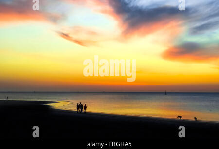 Silhouettes of people walking on the beach at sunset. Epic dramatic sunset.  Beautiful orange, yellow and blue colors sunset sky for background. Stock Photo