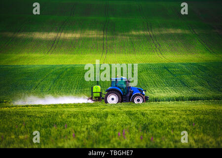 Farming tractor plowing and spraying on field Stock Photo