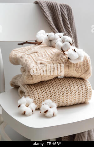 Knitted sweaters with cotton flowers on white chair Stock Photo