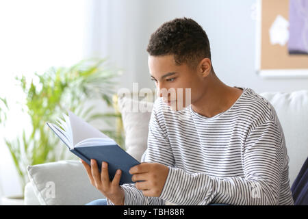 African-American teenage boy reading book at home Stock Photo