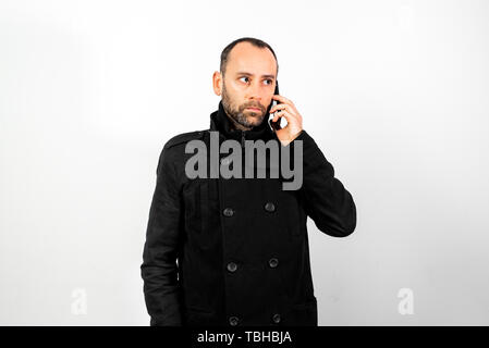Middle-aged man with overcoat listens attentively to a conversation on his mobile phone, isolated on white. Stock Photo