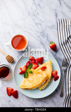Crepes, thin pancakes with cream cheese, ricotta and fresh strawberries. Marble background. Top view. Copy space. Stock Photo