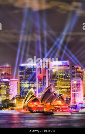 High-rise office towers of Sydney CBD skyline on waterfront of Sydney harbour during annual Vivid Sydney light show crossed by blue laser beams. Stock Photo