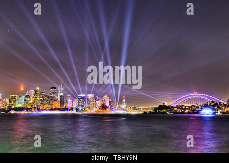 Skyline of Sydney city CBD on waterfront of Sydney harbour with arch of the Sydney harbour bridge under laser blue beams of Vivid Sydney light show. Stock Photo