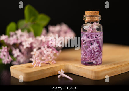 Lilac flowers and essential oil in a glass vessel. Ecological preparations on a wooden board. Dark background. Stock Photo