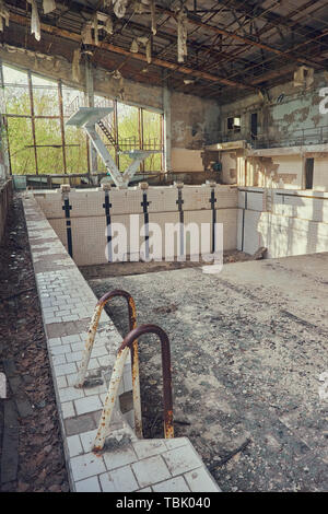 Abandoned swimming pool in Pripyat. Destroyed gym in a radioactive city. The street is overgrown with trees and bushes. Jumping tamplin. Stock Photo