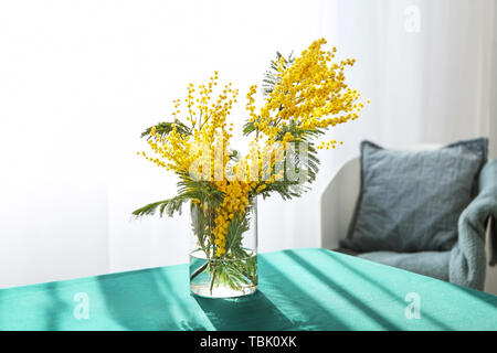 Vase with beautiful mimosa flowers on table in room Stock Photo