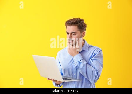 Thoughtful male programmer with laptop on color background Stock Photo