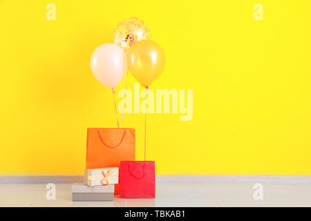 Beautiful gifts with air balloons on floor near color wall Stock Photo