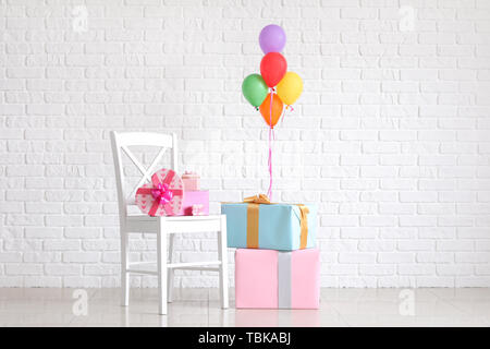 Beautiful gifts with air balloons near white brick wall Stock Photo