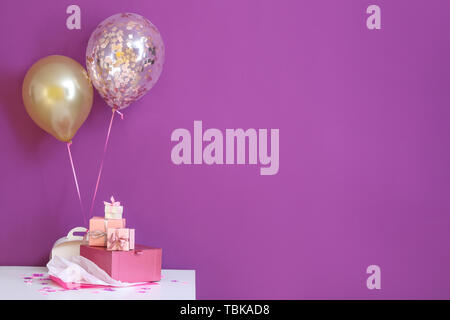 Beautiful gifts with air balloons on table against color background Stock Photo