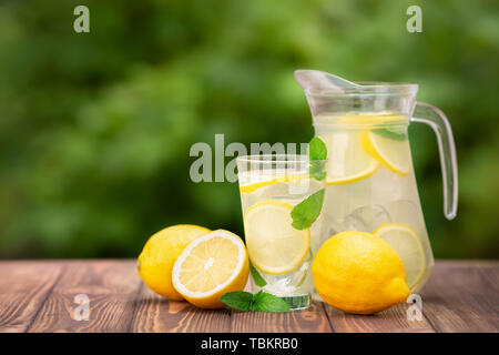 lemonade in glass and jug on wooden table outdoors. Summer refreshing drink. Cold detox water with lemon Stock Photo