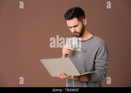 Thoughtful male programmer with laptop on color background Stock Photo